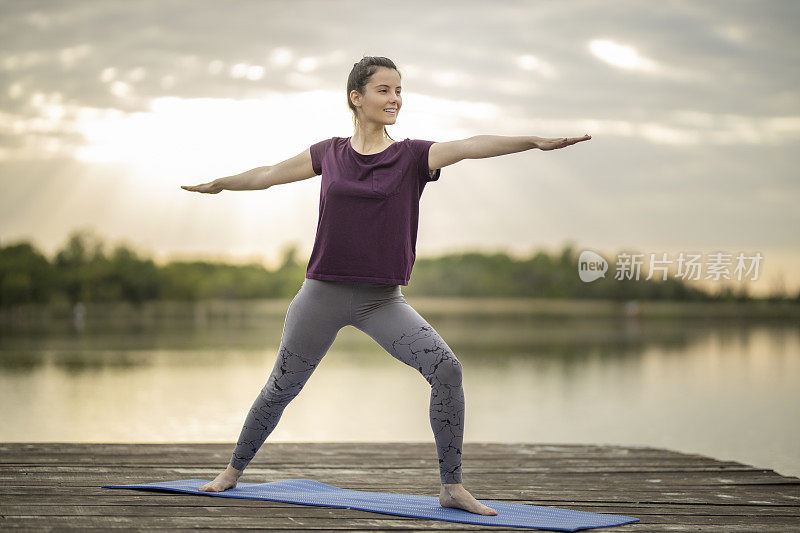 迷人的女人练习瑜伽，站在战士两个练习，Virabhadrasana II在湖码头pose